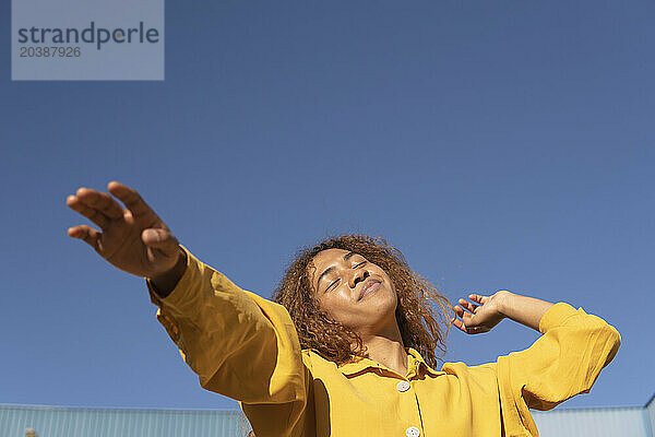 Smiling woman with eyes closed under clear blue sky on sunny day