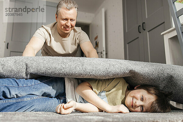 Playful father rolling son in carpet at home