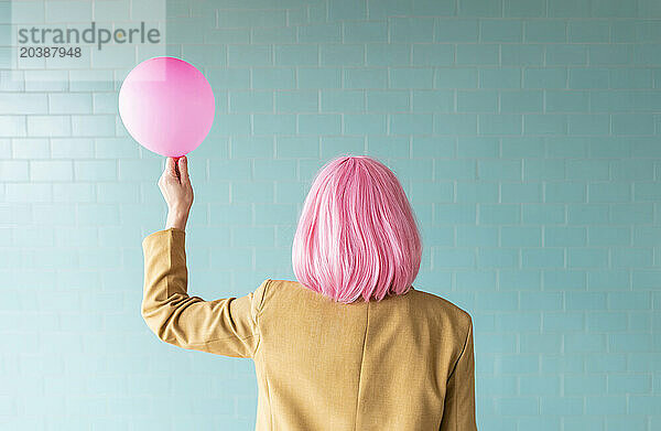 Woman with pink wig holding balloon near turquoise wall