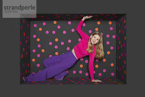 Blond teenager leaning in alcove over black background with colored dots