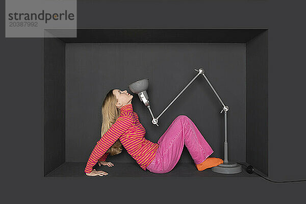 Teenage girl sitting in front of electric lamp by black background