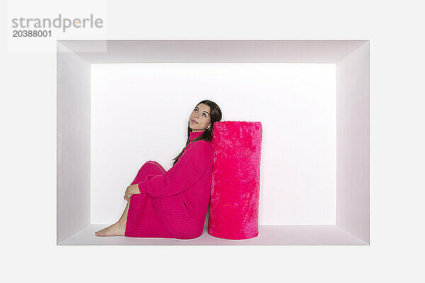 Thoughtful teenage girl leaning on pink bolster in alcove