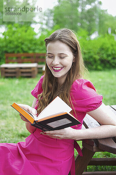 Smiling woman enjoying reading book at park