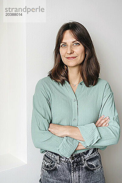 Smiling woman standing with arms crossed in front of wall