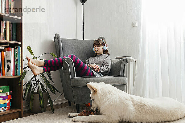 Girl listening to music through wireless headphones near dog in living room