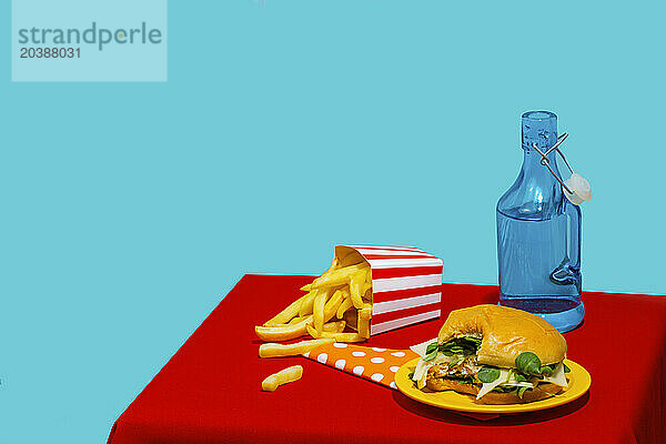 Bite taken from burger near french fries and soda bottle against blue background