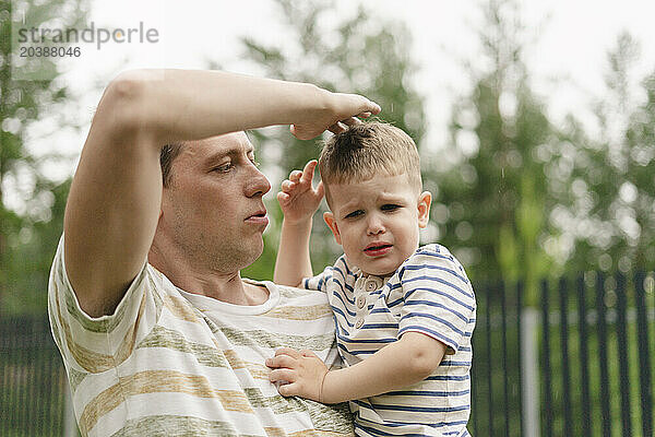 Father touching head of crying son in backyard