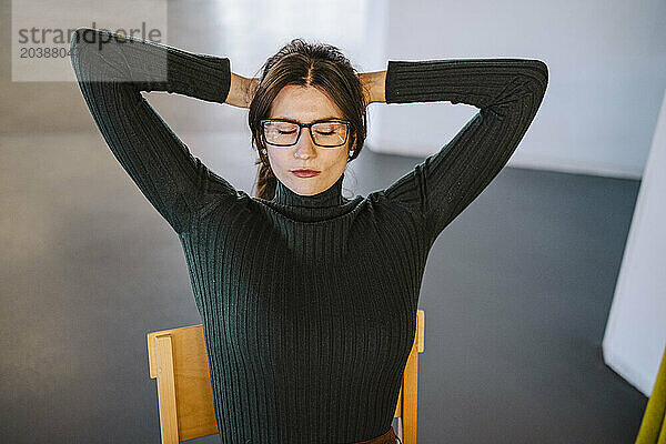 Businesswoman sitting with hands behind head in office