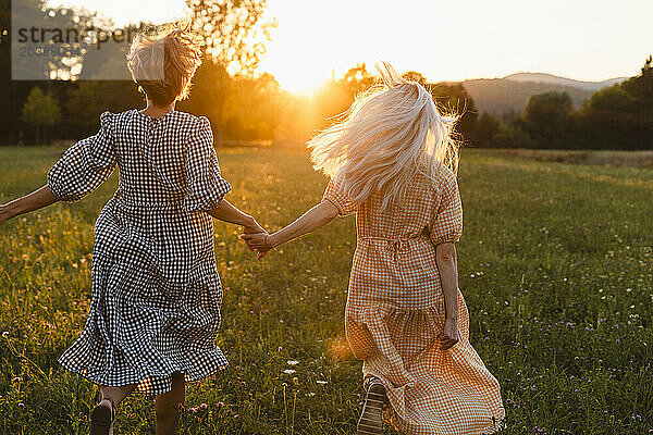 Carefree friends holding hands and running in park