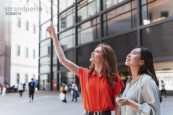 Woman pointing by friend standing near building in city