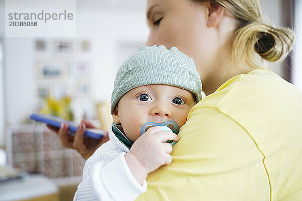 Mother carrying cute boy with pacifier at home