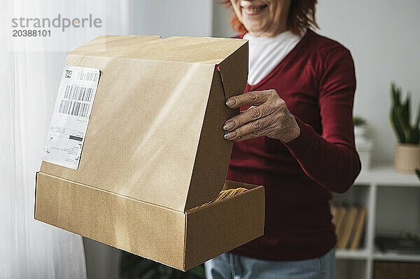 Retired senior woman opening cardboard package standing at home