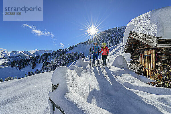 Mature couple back country skiing by snow covered cottage on sunny day  Schwalbenwand  Dienten Mountains  Salzburg  Austria
