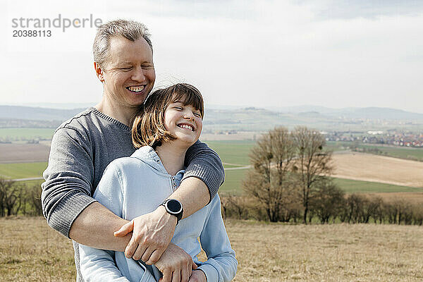 Happy man with arms around daughter standing on hill