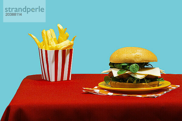 Cheeseburger with french fries on table against blue background