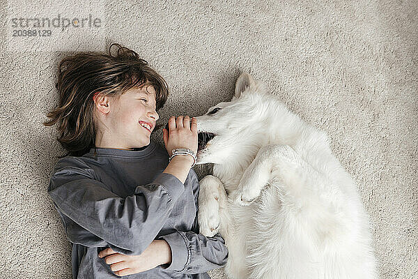 Happy girl playing with dog on carpet at home