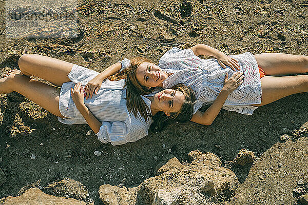 Smiling mother and daughter lying on sand