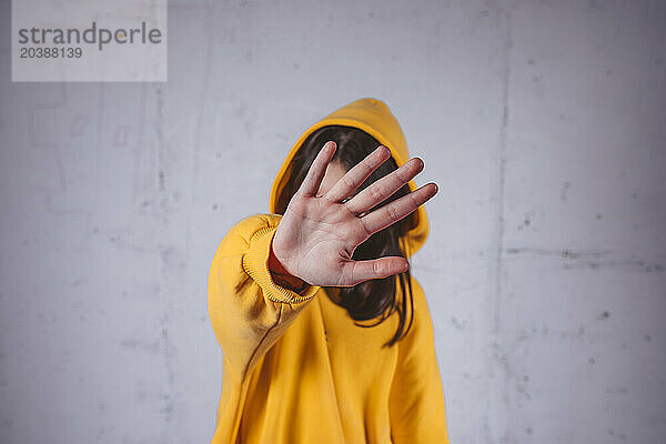 Girl in yellow hoodie covering face with hand in front of gray background