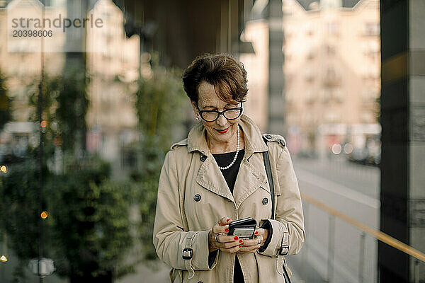 Retired senior woman using smart phone while walking on sidewalk