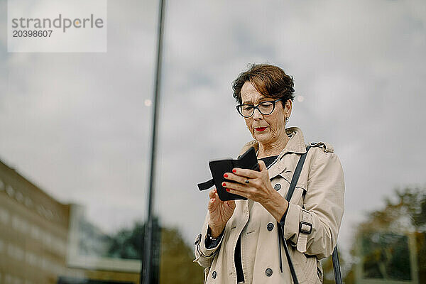 Retired senior woman using smart phone against glass wall