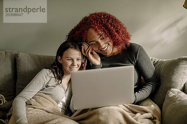 Smiling young woman and teenage girl watching movie together on laptop at home