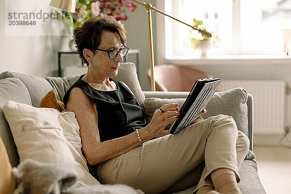 Retired senior woman using digital tablet while sitting on sofa at home