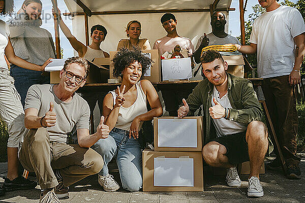 Group portrait of male and female volunteers gesturing while crouching by boxes at community center