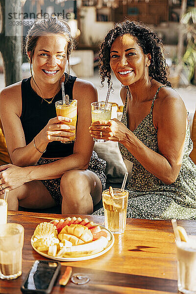 Portrait of smiling female friends enjoying healthy drinks while sitting at wellness resort