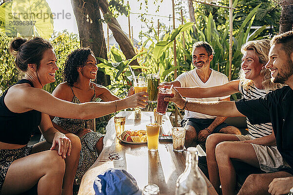 Smiling multiracial male and female friends toasting healthy drinks while sitting at wellness resort