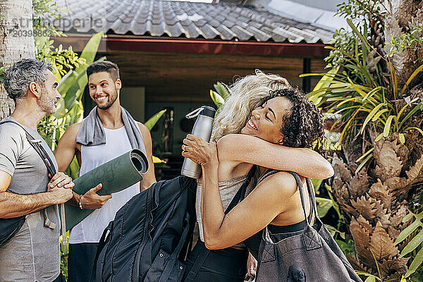 Happy women embracing each other while standing with male friends outside wellness resort