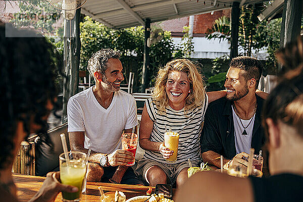 Happy woman enjoying smoothie with friends sitting at wellness resort