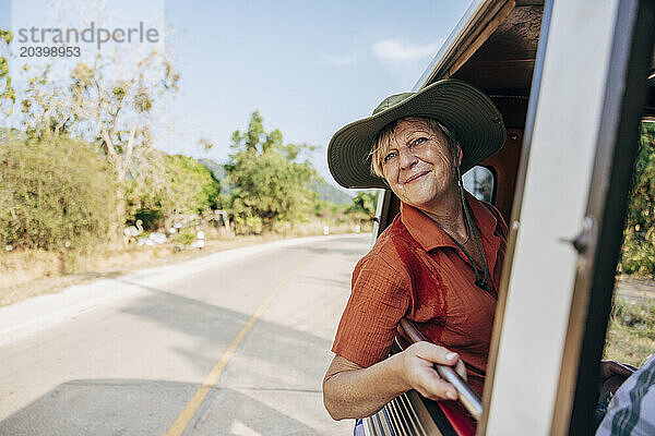 Smiling woman leaning out of window while sitting in tuk-tuk on vacation