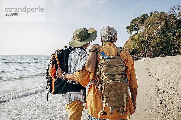 Rear view of senior gay couple with backpacks standing at beach on vacation