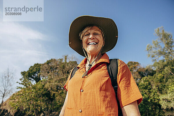 Low angle portrait of smiling senior woman wearing hat while standing against sky on vacation