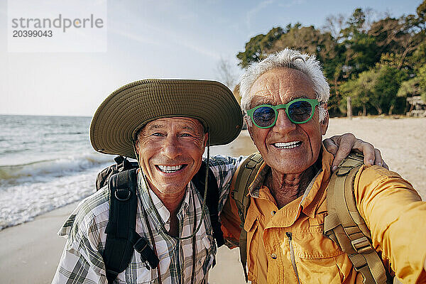 Portrait of smiling gay man taking selfie with boyfriend at beach on vacation