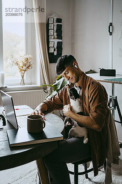 Smiling male freelancer sitting with pet dog at home office