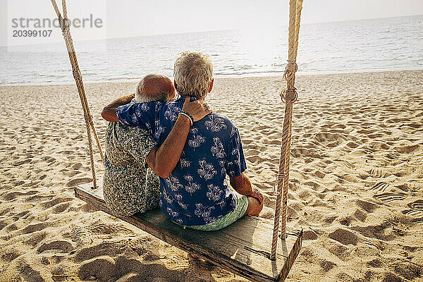 Romantic gay couple sitting on swing at beach