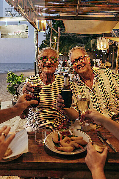 Portrait of senior male friends toasting drinks while sitting at beach restaurant