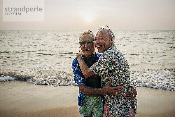 Cheerful senior gay couple embracing each other on vacation at beach