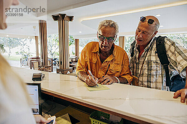 Senior gay couple filling form at reception desk in hotel