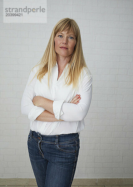 Beautiful blond woman standing with arms crossed in front of white wall