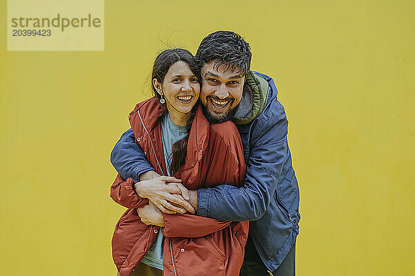 Happy mature man embracing woman against yellow background