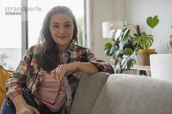 Mature woman with eyeglasses sitting on sofa in living room at home