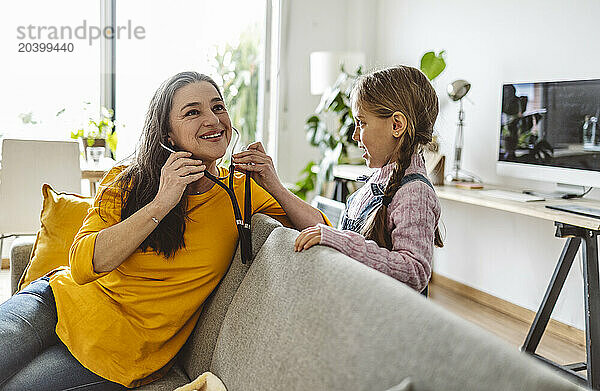 Smiling grandmother and granddaughter playing with stethoscope at home