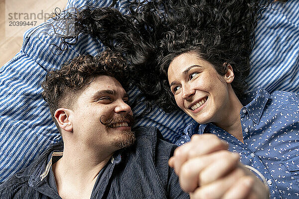 Smiling couple holding hands and lying on bed at home