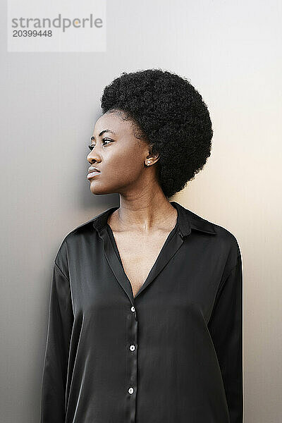 Thoughtful Afro woman standing near wall