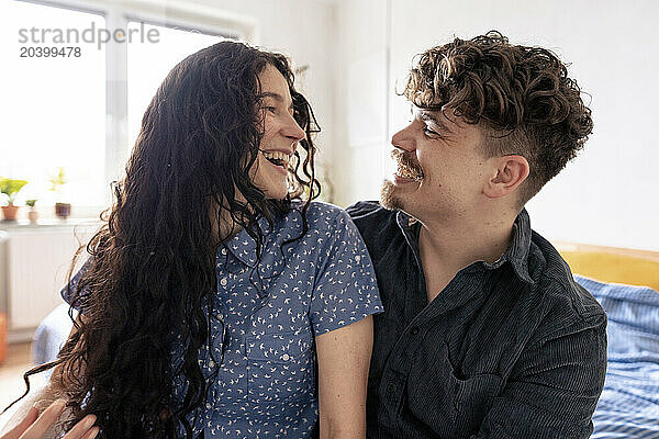 Happy couple looking at each other sitting in bedroom