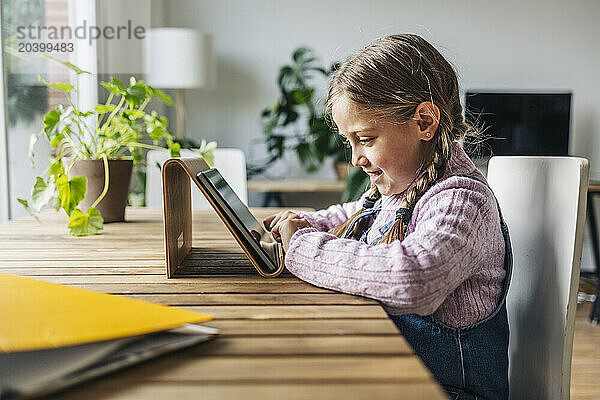 Girl sitting with tablet PC at table at home