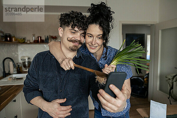 Smiling woman sharing smart phone with boyfriend in kitchen at home