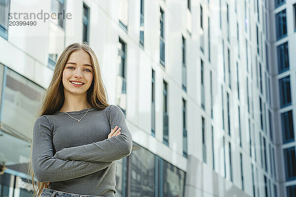 Smiling beautiful teenage girl with arms crossed in front of building